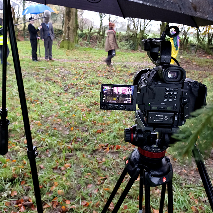 Image of camera filming people on location in a field.